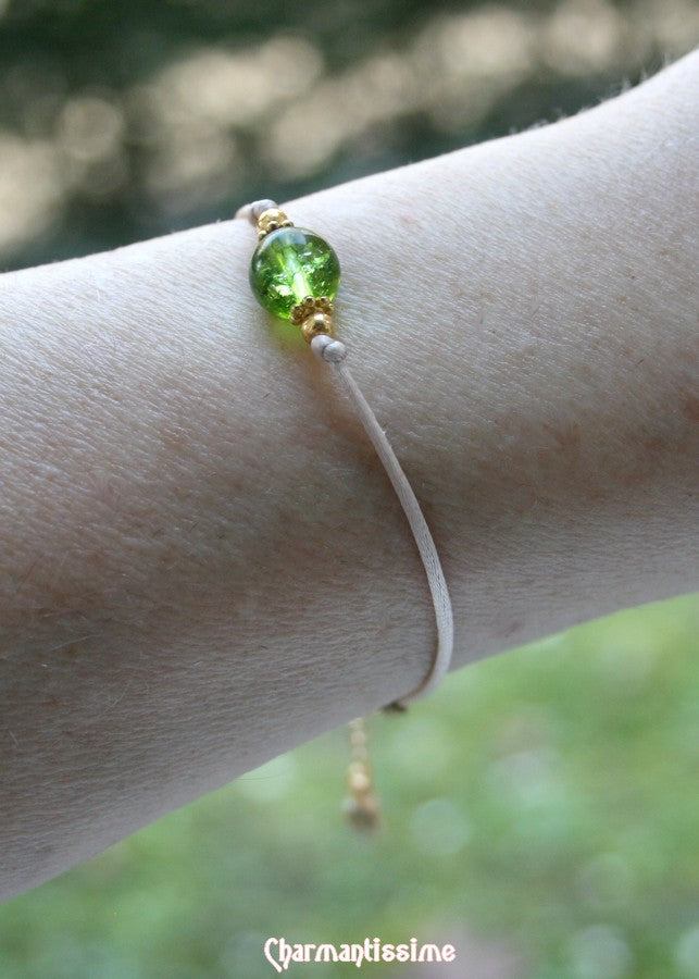 Bracelet très féminin, baroque romantique et raffiné, tendance boho-chic en perle naturelle de péridot vert ornée de fines perles laiton doré. Ce charmant bijou est monté sur un cordon fin satin beige ajustable grâce à une fine chainette d'extension en laiton plaqué or avec petit strass vert en breloque.